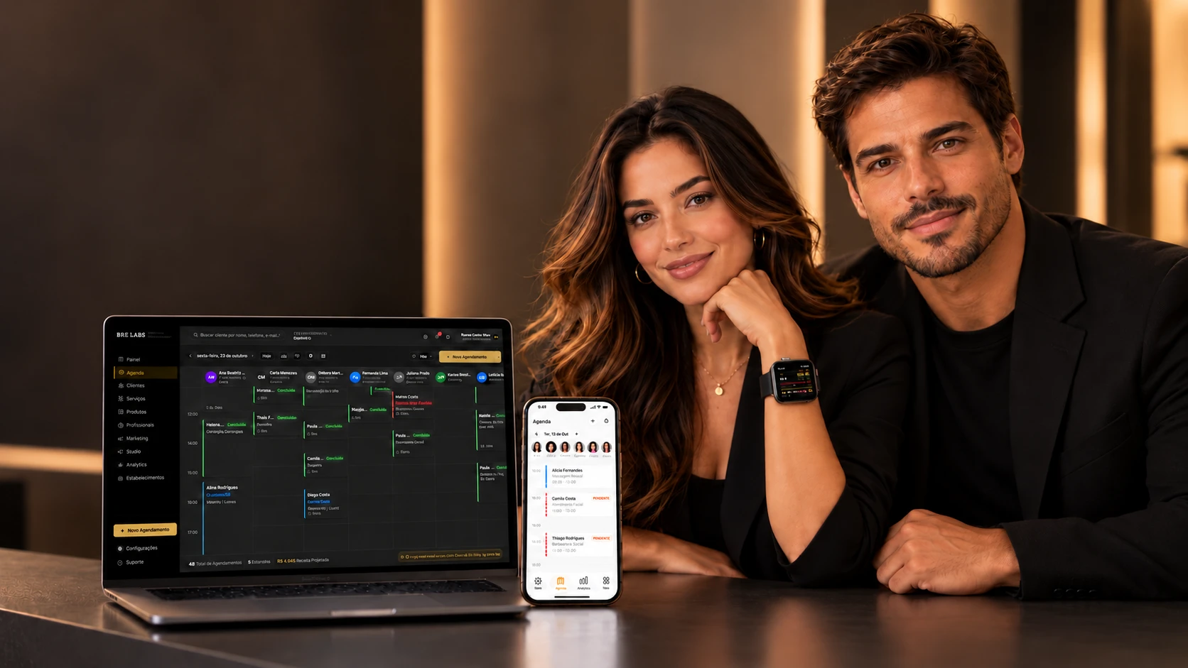 Casal de profissionais de beleza sorrindo ao lado de um notebook e de um celular mostrando a agenda da BRE